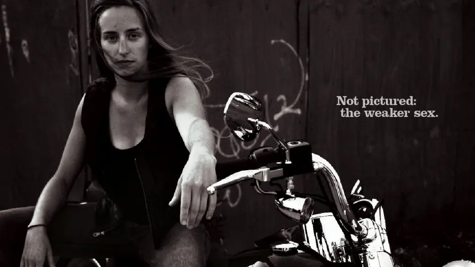 A black and white portrait of a woman on a motorcycle with the line: Not pictured, the weaker sex.