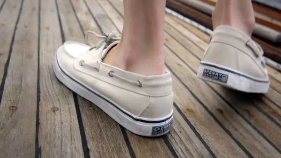 White Sperry boat shoes on a wooden deck.