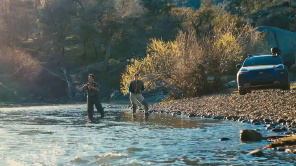 People fishing in a river beside a Subaru.