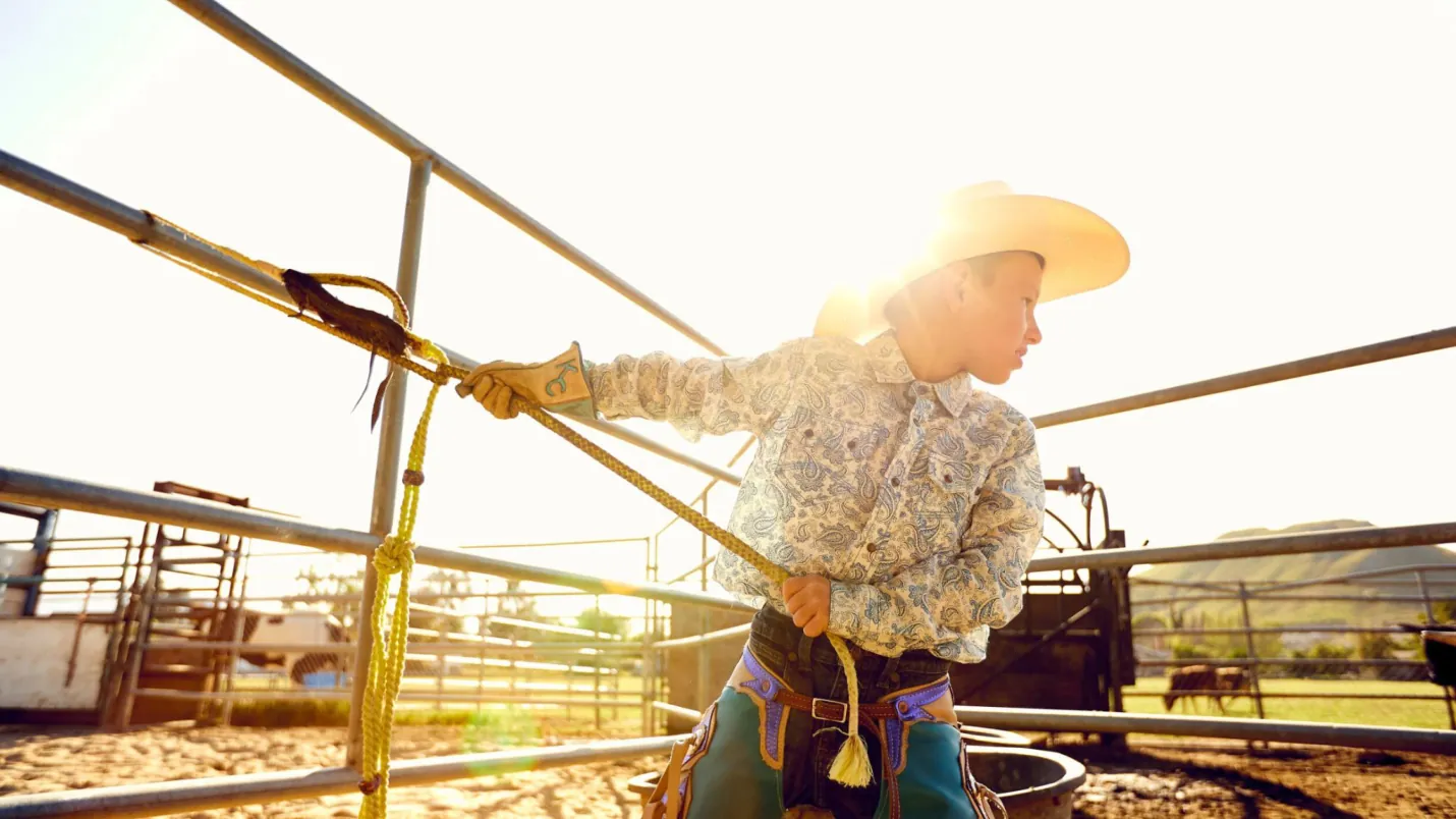 A young rider in a cowboy hat at the chutes at sunset.