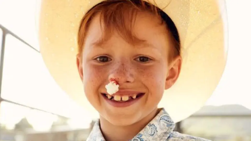 A smiling red-haired boy in a cowboy hat.